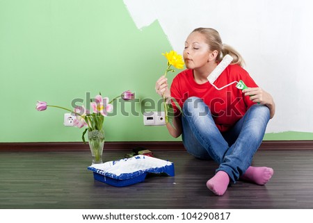 Young woman with flower and paint roller in hands painting interior wall