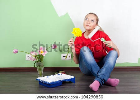 Young woman with flower and paint roller in hands painting interior wall of home