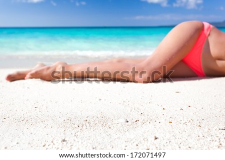 Tan slim legs lying on white sandy beach near sea, no face