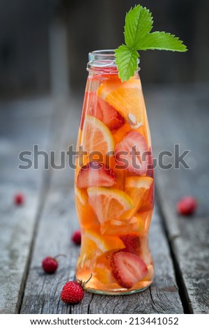 Bottle with sliced oranges and strawberries on wooden table, organic vegan drink