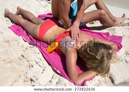 Man applying SPF sign with sun protection lotion on a woman back, summer tropical beach vacation