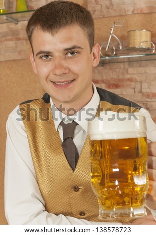 The waiter holds out hand forward with glass of of beer