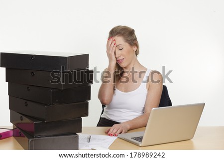 Image of a young female executive tired of work piling up on her desk, many files and folders on the desk, isolated on white background.