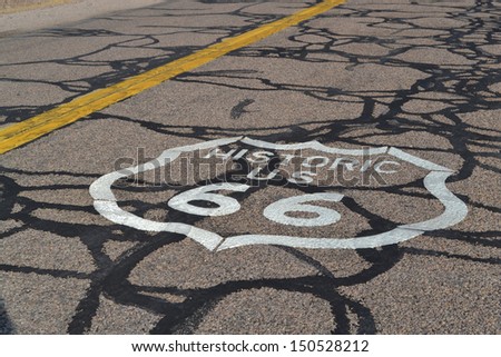 Cracked old endless road with yellow double line and Route 66 sign in the Arizona desert, USA