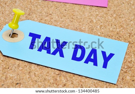 a paper label with the words tax day written on it, pinned with a thumb tack on a cork board