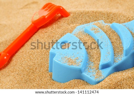 a blue fish-shaped mold and an orange toy shovel on the sand