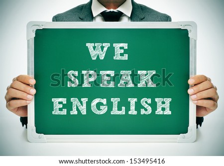 a man wearing a suit holding a chalkboard with the sentence we speak english written in it