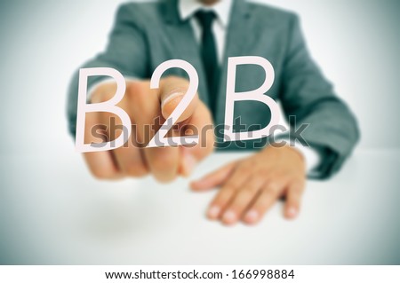 man wearing a suit sitting in a table pointing to the word B2B, business-to-business, written in the foreground