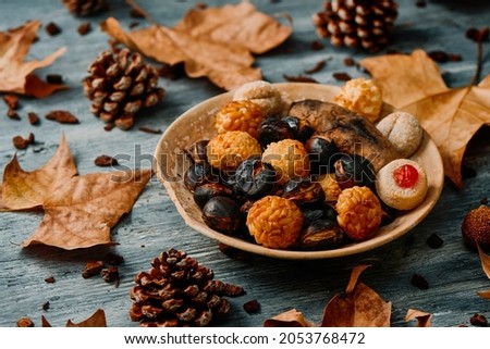 a plate with a roasted sweet potato, some roasted chestnuts and some panellets, typical confection of Catalonia, Spain, eaten traditionally in All Saints Day, in a party called Castanada, on a table