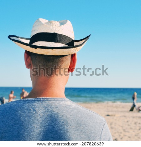 back view of a young man with a straw hat hanging out on the beach