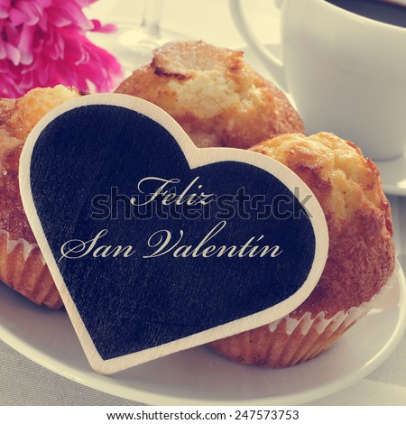 the text feliz san valentin, happy valentines day in spanish, written in a heart-shaped signboard, in a plate with magdalenas, spanish plain muffins