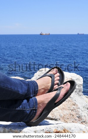 closeup of the feet of a man with flip-flops who is relaxing near the ocean in the summer