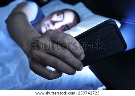 closeup of a young man in bed looking at the smartphone at night