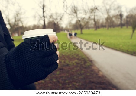 closeup of a young caucasian man very sheltered wearing fingerless gloves holds a hot drink in a paper cup in Hyde Park in winter in London, United Kingdom