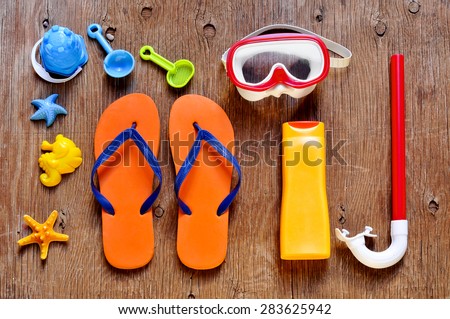 high-angle shot of a rustic wooden table full of summer stuff, such as a starfish, a diving mask and a snorkel, a bottle of sunblock, a pair of flip-flops and some beach toys