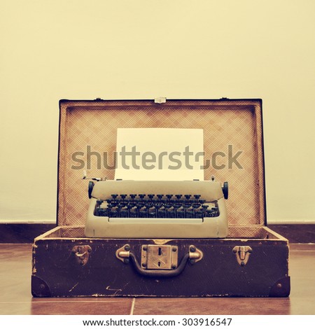an old typewriter with a blank page in its roller, placed in an old suitcase, with a retro effect