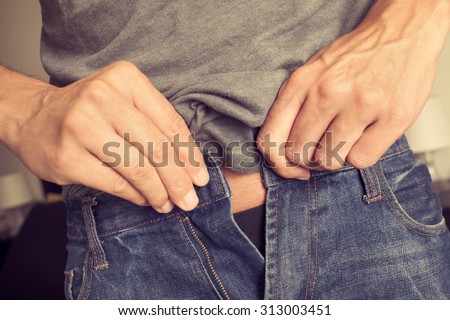 closeup of a young man trying to fasten his trousers, because of the weight gain