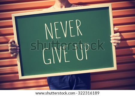 closeup of a young caucasian man showing a chalkboard with the text never give up, with a slight vignette added