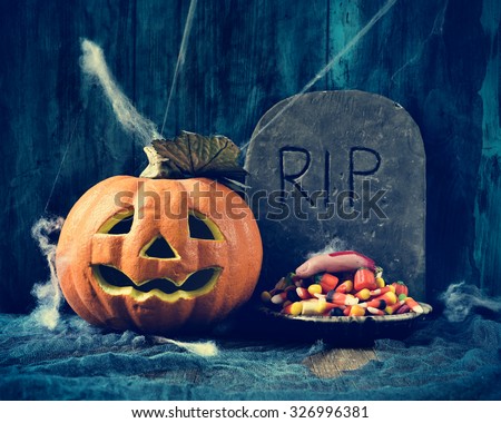 a plate with Halloween candies and an amputated finger in a dismal scene with a carved pumpkin and a gravestone with the text RIP carved in