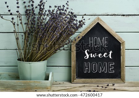 closeup of a house-shaped chalkboard with the text home sweet home written in it and a bunch of lavender flowers in a flower pot, against a rustic pale blue background 商業照片 © 