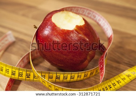 Bite on red apple with measuring tape on wooden table.