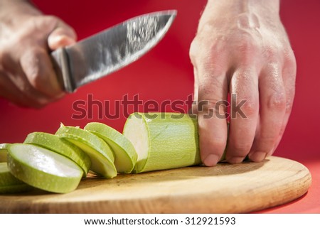 Unrecognizable man chopping zucchini with a kitchen knife on cutting board.