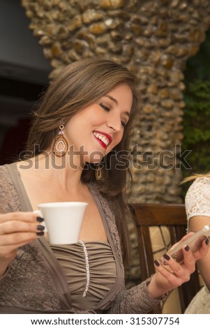 Beautiful young woman using cell phone and typing text message while sitting cafe.