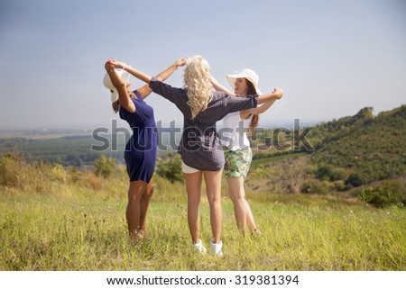 Three cheerful young women spending a day in nature. They are standing and holding hands in unity and celebrating their friendship.