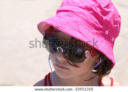 a young caucasian girl relaxed at the beach listening to music with earphones in her ears and wearing a hat to protect herself from the damage of the sun