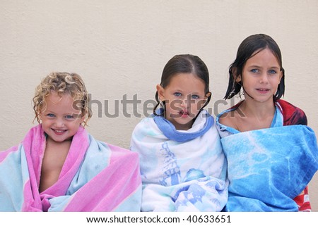 three caucasian sisters with blue eyes wrapped up in a beach towel all with different expressions on their faces
