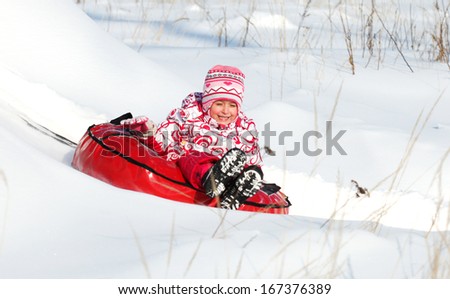 little girl with snow slides down a hill on the tubing