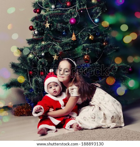 little girl and her little brother sitting under the Christmas tree