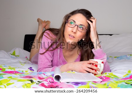 young woman thinking in bed with magazine and coffee