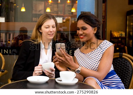 two ladies sitting outside a coffee shop looking at their phone