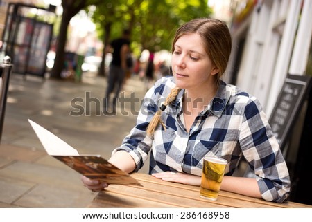 young woman sitting outside a bar with a drink and menu