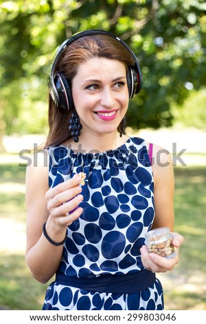 young woman in the park eating nuts and listening to music