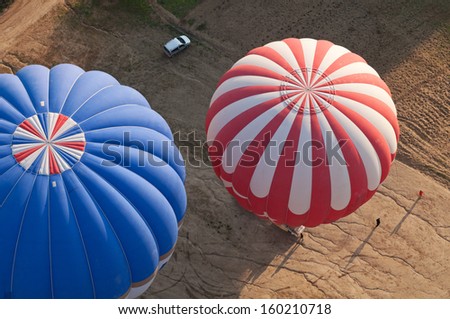 The top view on two balloons landing in the field. Near them people who help landing of balloons, and the car.