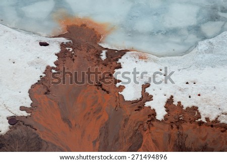 Bizarre streams of bright red clay on  ice of  lake near shore.