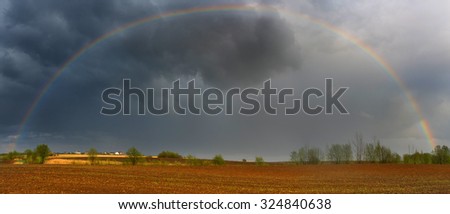 Panorama of the plowed field with thunderclouds and a rainbow.