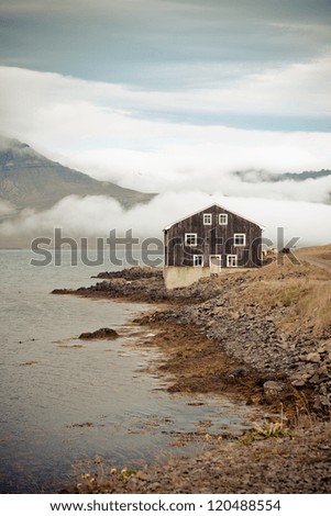 Lonely Black Wooden House at coastline ?in East Iceland. Vertical toned shot