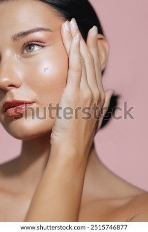 Stunning Latina woman with radiant skin and natural makeup poses with her hand gently touching her face in this close-up portrait against a pink background. Ideal for skincare promotions, beauty