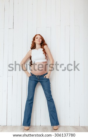 Studio portrait of beautiful slim sexy pregnant woman wearing casual jeans over wooden white background