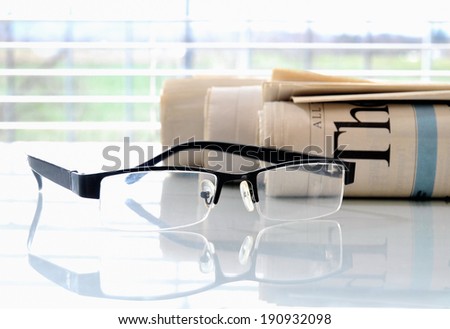 Rolled newspapers with glasses in front of a window