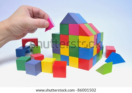 Human hand and house of multicolored toy blocks on white background