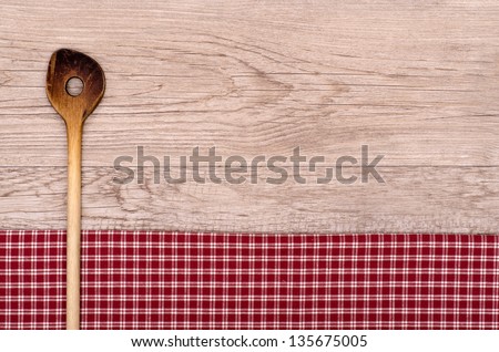 Old cooking spoon on checkered table cloth and wooden board