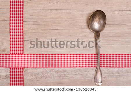 Silver spoon an red checkered ribbon on wooden board