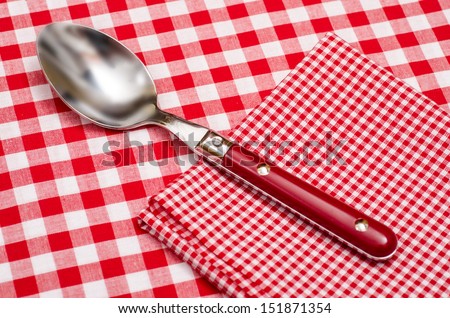 Spoon and napkin with red and white checks on a table cloth