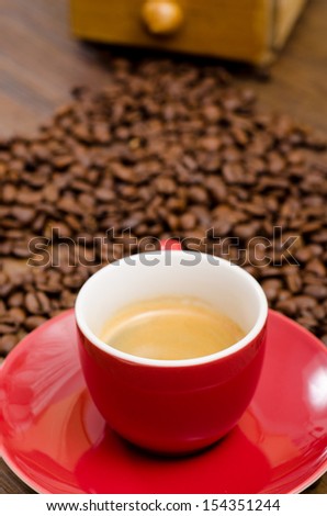 Espresso coffe in a red mug in front of brown coffee beans