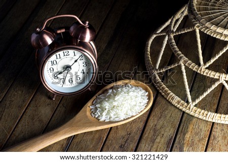 Alarm Clock of copper  color and rice in wood spoon and wood basket on wood background.