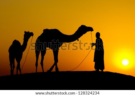 Rajasthan village. Silhouette of a man and two camels at sunset in the desert, Jaisalmer - India